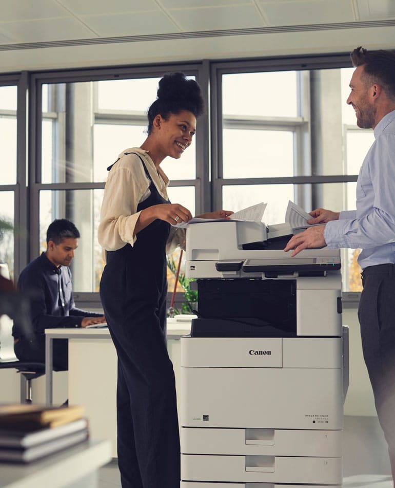 Colleagues collecting documents at a Canon imageRUNNER ADVANCE multifunction printer in a modern office